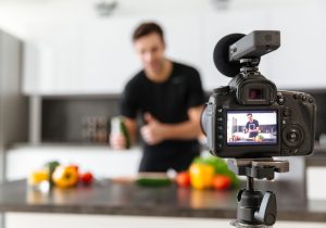 Close up of a video camera filming young smiling male blogger at the kitchen